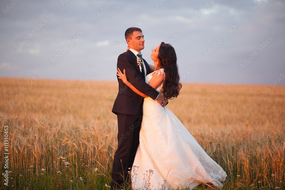 Beautiful romantic wedding couple of newlyweds hugging in park on sunset
