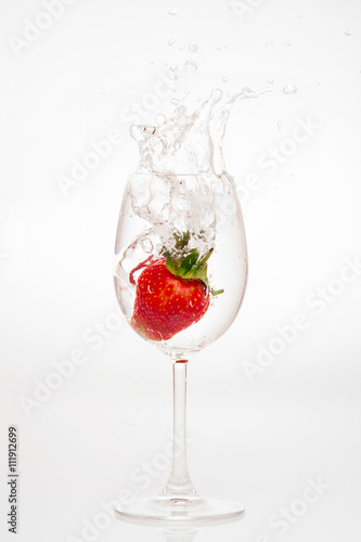 splashing strawberry into water glass on white background