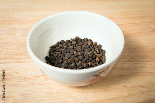 bowl of black dried pepper on a wood background