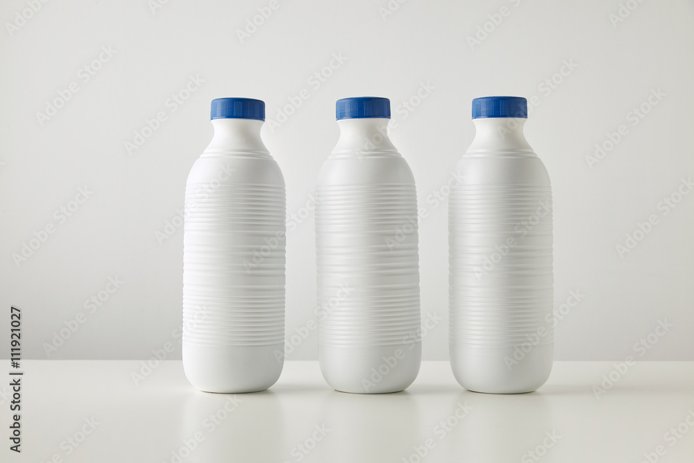 Three blank white plastic riffled bottles with blue caps in row isolated on table in center Space for your text Merchandise retail set, rich texture Three blank white plastic riffled bottles with blue caps in row isolated on table in center Space for your text Merchandise retail set, rich texture