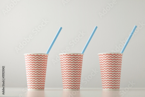 Retail set of three paper cups decorated with red line pattern and with blue drinking straw inside isolated on white table Place for your text above