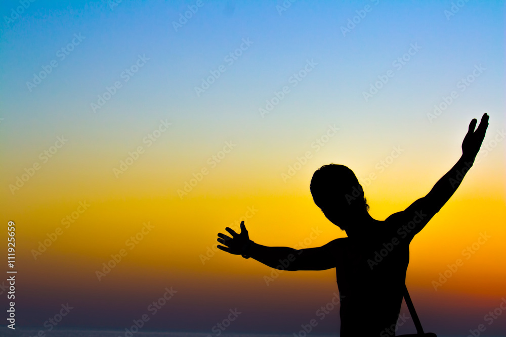 Young man standing with arms outstretched at sunset