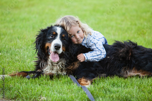 cute boy with curly blonde hair embraces a bernese mountain dog
