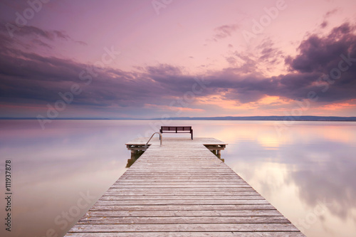alter Holzsteg mit Bank am See zum Sonnenuntergang