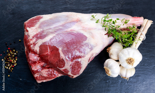 Quadro em tela Raw lamb leg on blue stone background with herbs