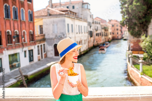 Young female traveler eating traditional italian bolognese pasta to go on the bridge in Venice. Image with small depth of field