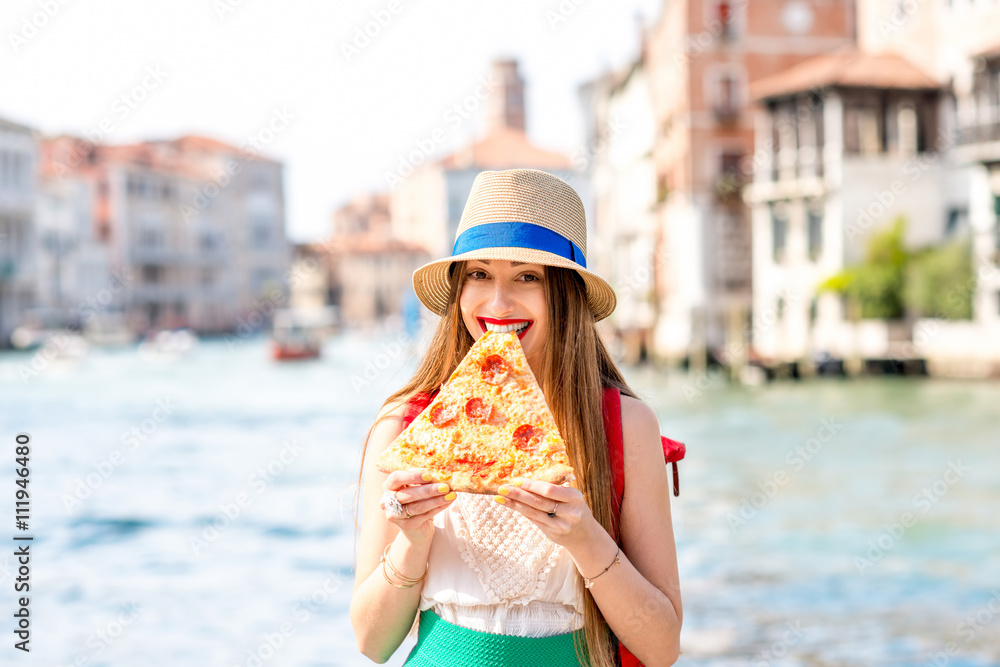 Young female traveler eating traditional italian pizza slice on the water canal background in Venice.