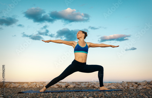 Woman practicing yoga outdoors over sunset sky background