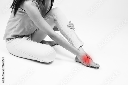 Foto Young woman sitting on ground touching her injured foot on white