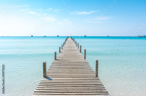 Wooden bridge on the beach to the sea in blue summer sky.  Jetty