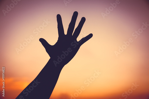 Silhouette of a hand on colorful sunset sky background.