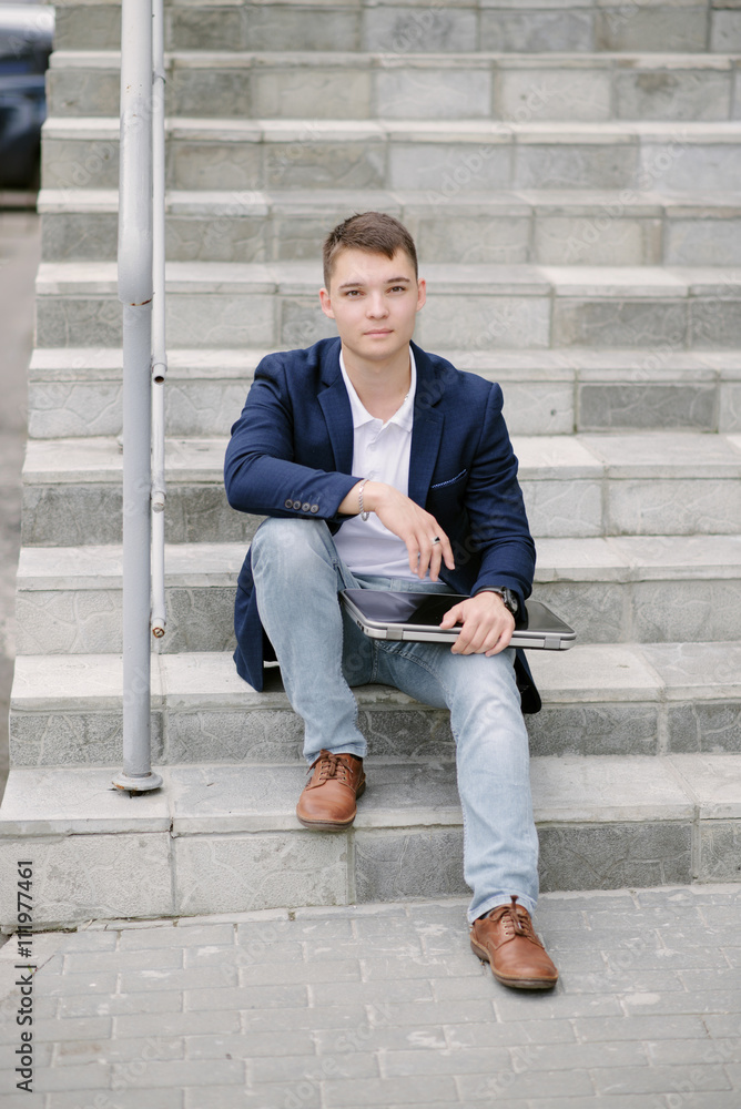 Portrait of a young businessman sitting with notebook on stairs. Portrait of a young businessman sitting with notebook on stairs.