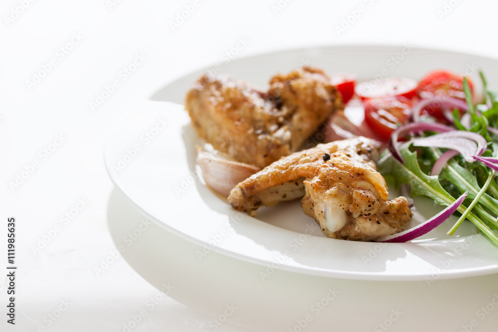 Homemade tasty roasted chicken wings with vegetables on a white plate, closeup Homemade tasty roasted chicken wings with vegetables on a white plate, closeup