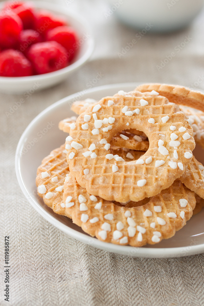 Cookies with sugar drops on a white plate with raspberries on a background on a linen textile, closeup Cookies with sugar drops on a white plate with raspberries on a background on a linen textile, closeup