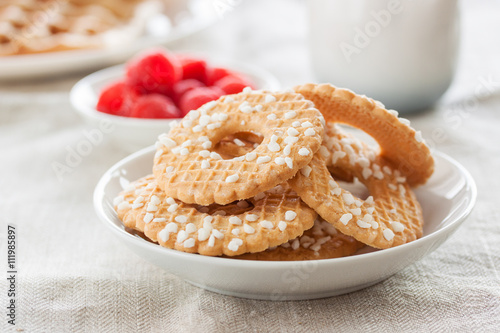 Cookies with sugar drops on a white plate with raspberries on a background on a linen textile, closeup