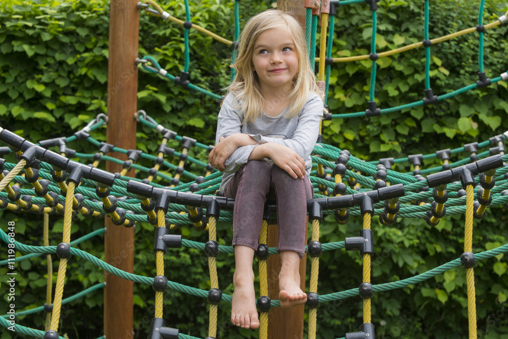 Portrait of Happy little blond girl playing on a rope web playground outdoor