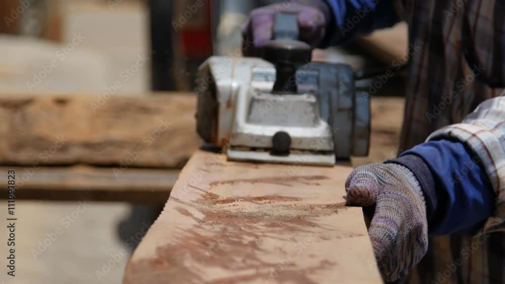 worker planing a plank of wood with a electric planed worker planing a plank of wood with a electric planed