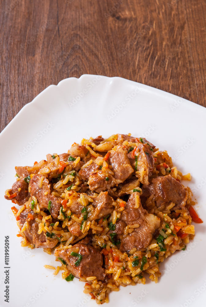 Rice with meat and vegetables in a plate on wooden table Rice with meat and vegetables in a plate on wooden table