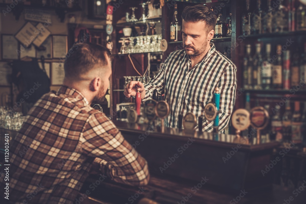 Handsome bartender pouring a pint of beer to customer in a pub.