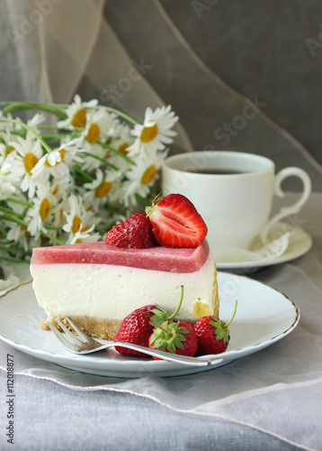 A piece of  cake, white cup of tea and strawberries..
