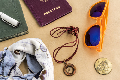 Travel concept with bandanna, sunglasses, coins, compass with string, journal and passport objects on top of yellow surface