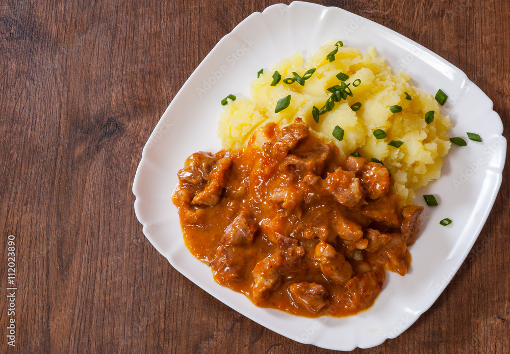 meat in sauce with mashed potatoes in a plate on wooden table