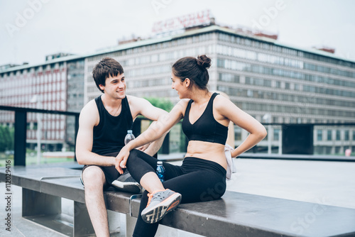 Couple of young handsome caucasian sportive man and woman having a break after training, drinking water and drying themselves with a towel, chatting - sportive, fitness, health concept