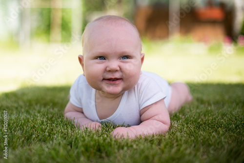 baby is lying on the grass in the garden and smiling
