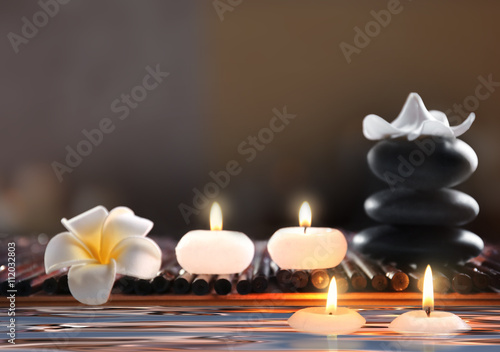 Composition with spa stones  flower and candles in water on blurred background