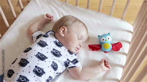 Baby sleeping with a toy owlet in a bedroom. One year old boy sleeping in his bed on the white sheet. Day child sleep