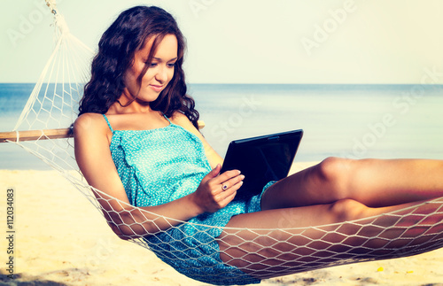 Young woman relaxing on hammock and using digital tablet. Vacation and travel concept photo