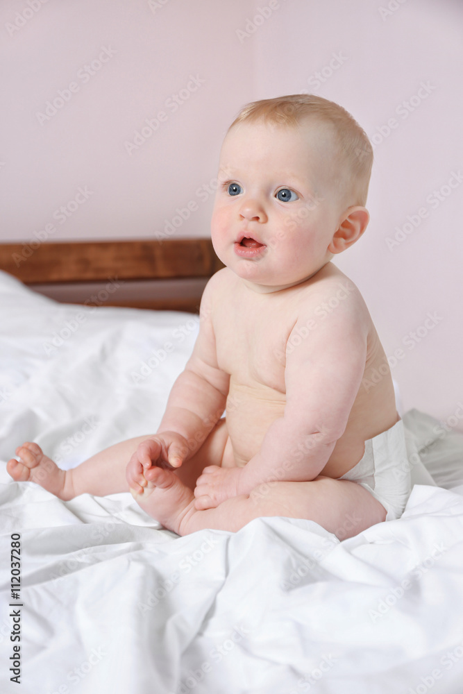 Adorable baby sitting on parents bed, close up Adorable baby sitting on parents bed, close up