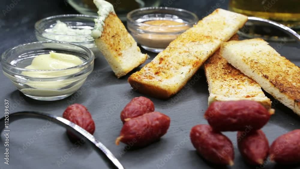 A glass with beer and snacks on a plate on a dark table. A plate of sausages , toast and sauce to beer. View of beer and snacks rotation 360 close up