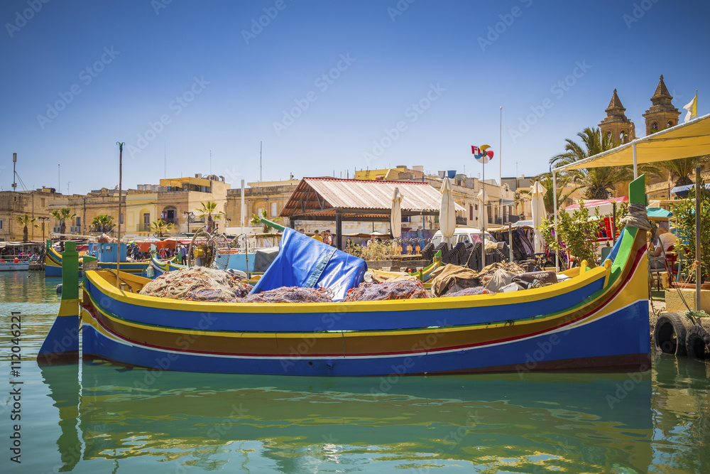 Malta - Traditional colorful Luzzu fishing boat at Marsaxlokk on a nice summer day with blue sky and crystal clear sea