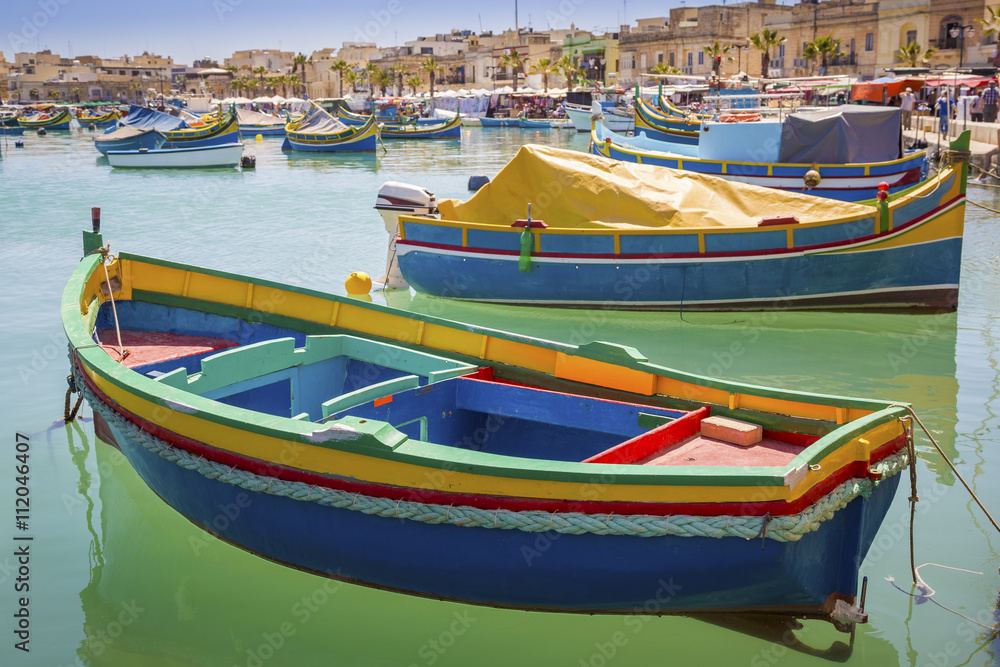 Malta - Traditional colorful Luzzu fishing boats at Marsaxlokk on a nice summer day with blue sky and crystal clear green sea