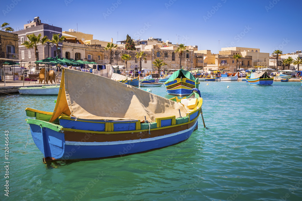 Malta - Traditional colorful Luzzu fishing boats at Marsaxlokk on a nice summer day with blue sky and crystal clear sea
