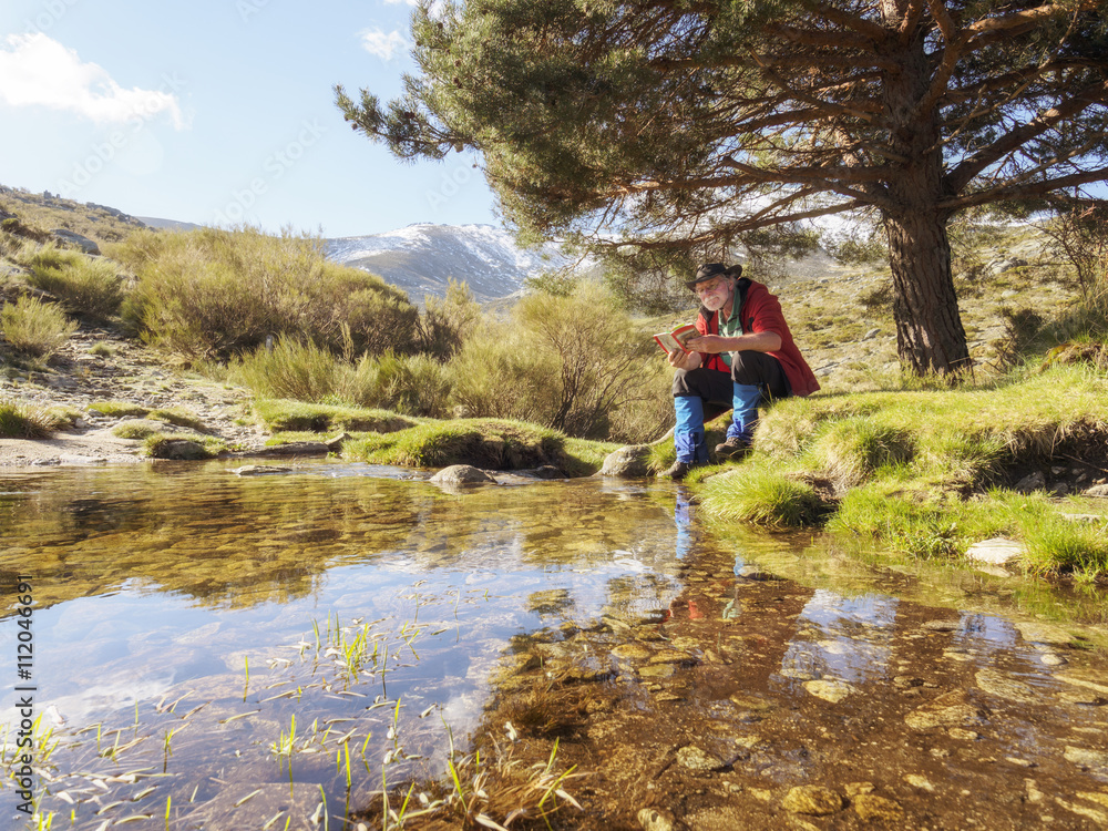 Spain, Sierra de Gredos, Hiker sitting at lake reading a book Spain, Sierra de Gredos, Hiker sitting at lake reading a book