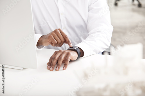 Man's hand adjusting smartwatch at desk photo