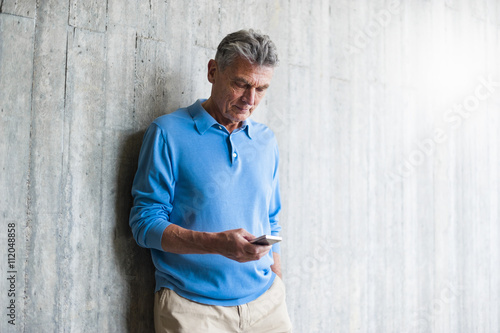 Senior man at concrete wall looking on cell phone photo