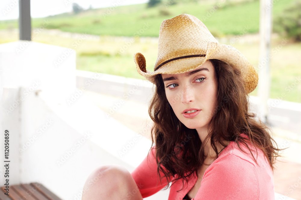 Serious young woman sitting outside in hat