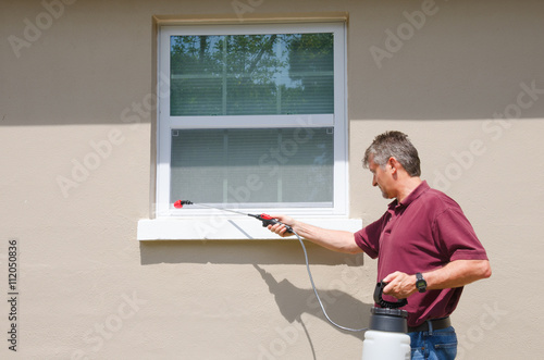 A professional pest control service man or do-it-yourself home owner spraying pesticide on the outside of house to keep bugs out.