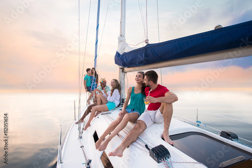 Young people sitting on yacht. Guys and girls laughing. Laughter prolongs life. Happy and healthy youth.