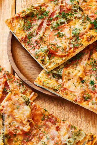 Slices of a traditional pizza with ham, cheese and tomatoes sprinkled with herbs on wooden plate