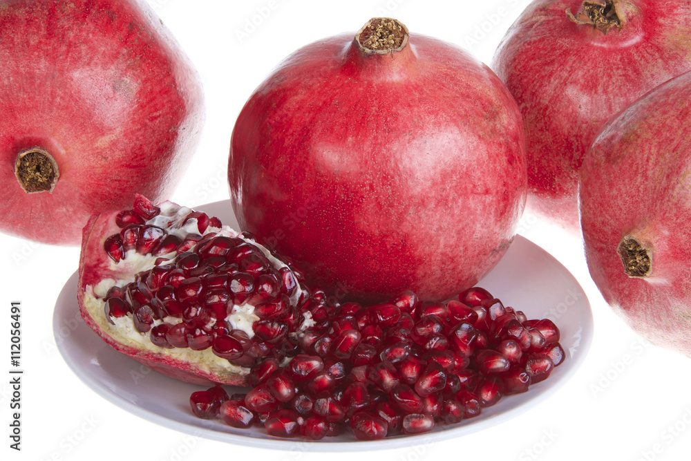 pomegranates, botanical name Punica granatum. Served on a plate with whole fruit in background, Isolated on white background. pomegranates, botanical name Punica granatum. Served on a plate with whole fruit in background, Isolated on white background.