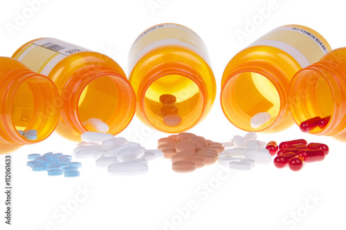 Five Prescription bottles lined up on their sides spilling medication pills out onto a white table surface isolated on a white background. Depicting multiple medications, overwhelming to keep track of photo