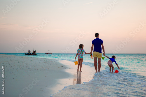 Father and kids walking on white sandy beach
