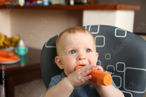 Baby eating carrot in a chair