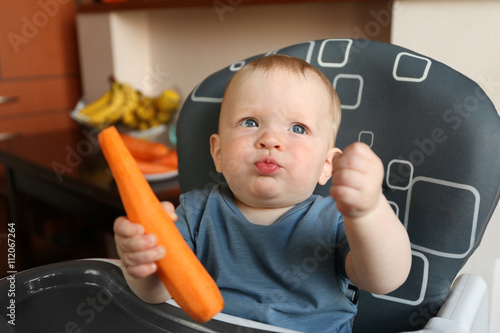 Baby eating carrot in a chair