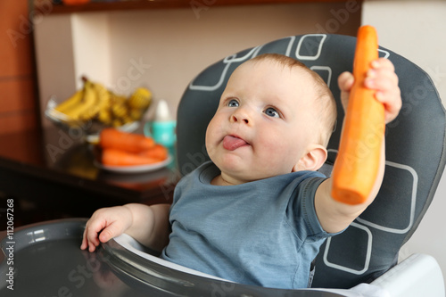 Baby holding carrot in a chair