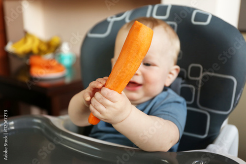 Baby holding carrot in a chair
